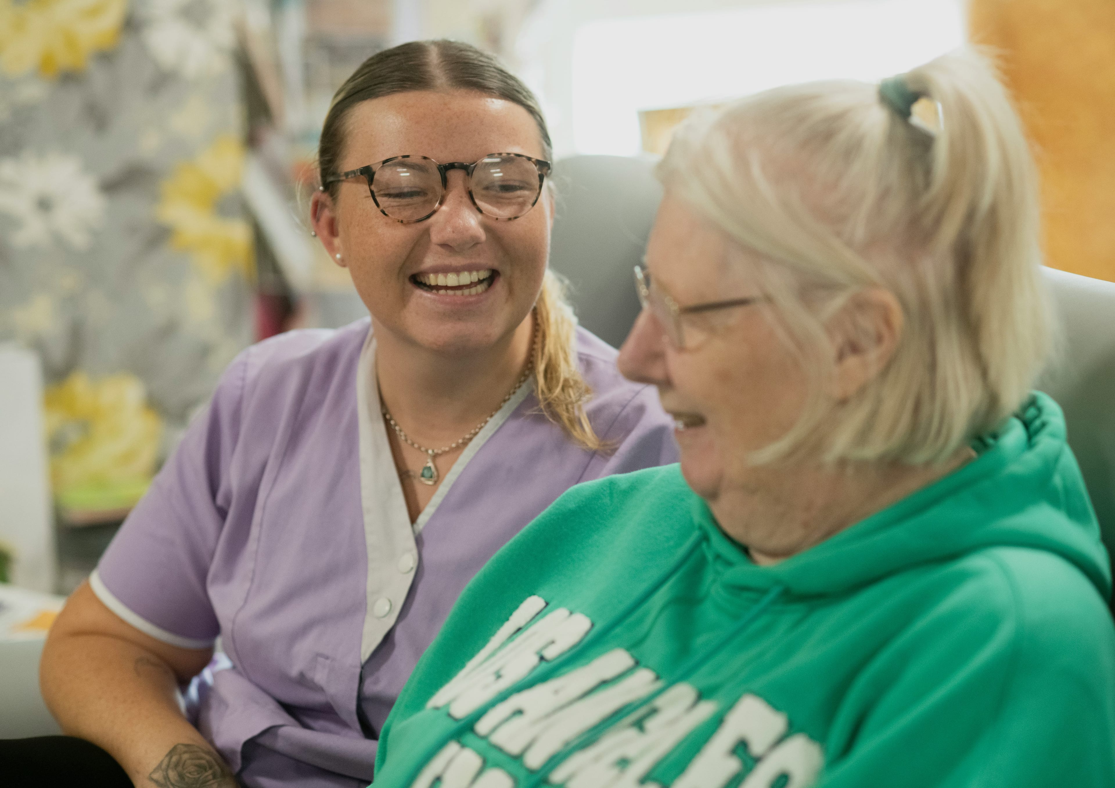 An Abundance Living caregiver in scrubs laughing with an elderly client during a home care visit in Boise, Idaho