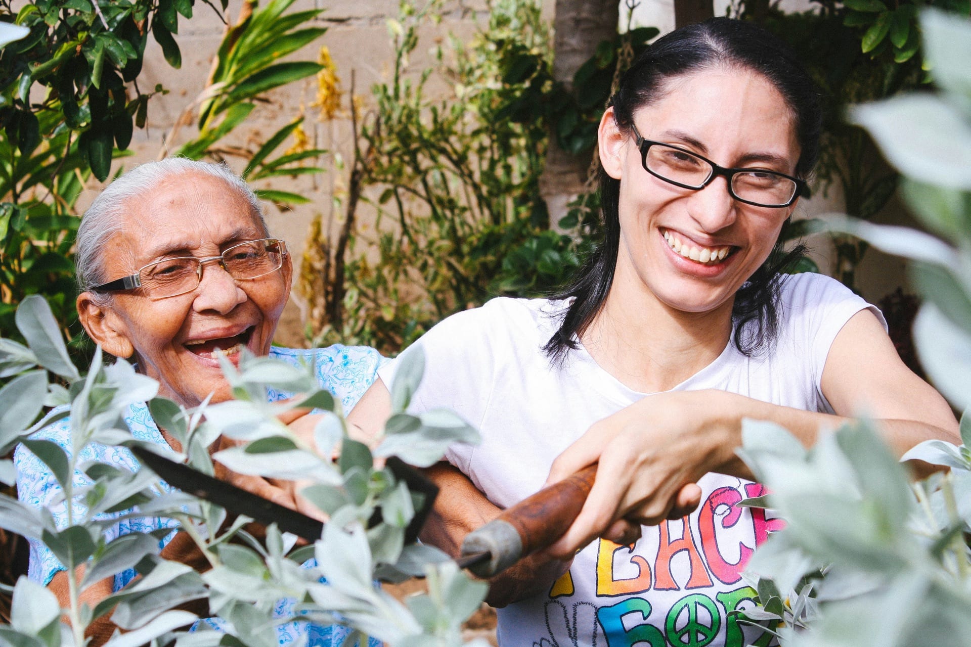 A caregiver and older adult laughing together while gardening outdoors
